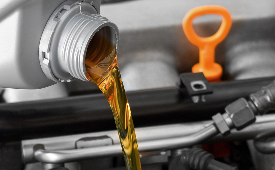 motor oil being poured into a car engine, next to an orange dipstick handle